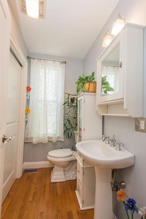 half bath with baseboards, toilet, and wood finished floors
