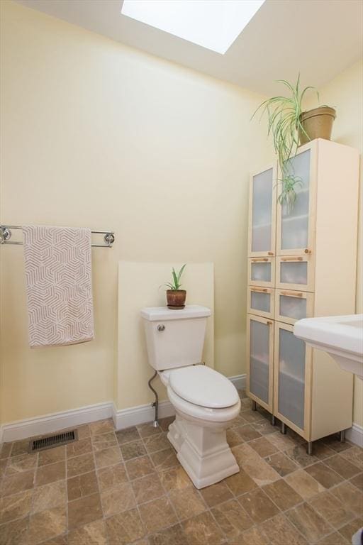half bath with toilet, baseboards, stone finish flooring, a skylight, and visible vents
