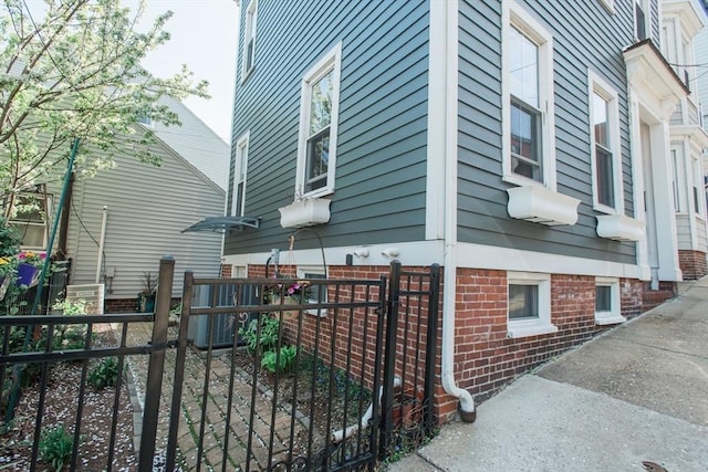 view of property exterior featuring brick siding, fence, and a gate