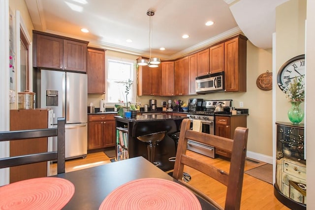 kitchen with dark countertops, appliances with stainless steel finishes, light wood finished floors, a center island, and ornamental molding