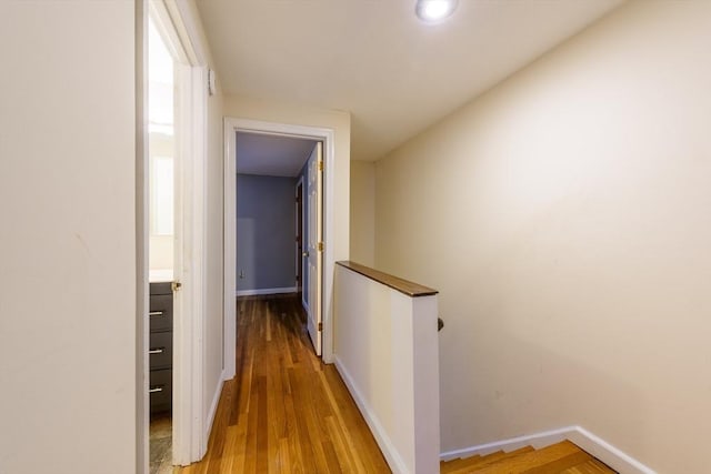 hallway with baseboards, wood finished floors, and an upstairs landing