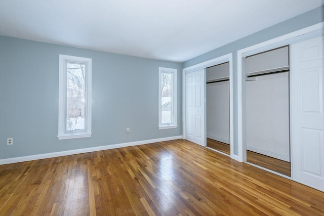 unfurnished bedroom with baseboards, two closets, and wood finished floors