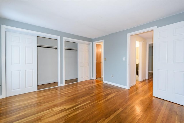 unfurnished bedroom featuring multiple closets, light wood-style flooring, and baseboards