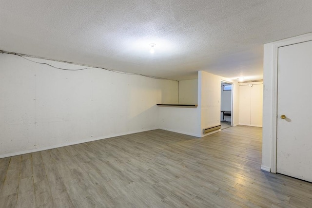 finished below grade area with light wood-style flooring, baseboards, and a textured ceiling