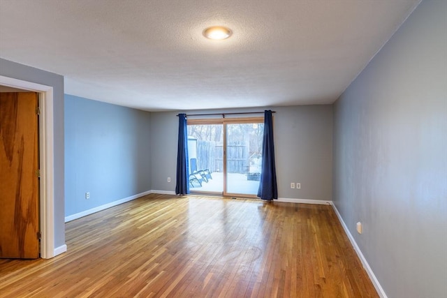 spare room with a textured ceiling, wood finished floors, and baseboards