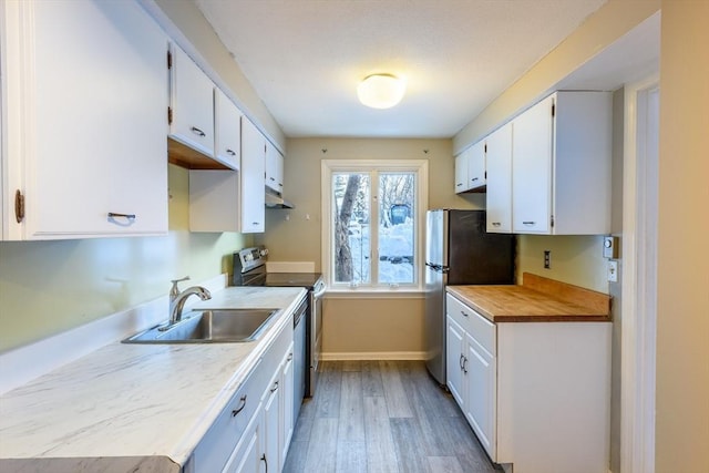 kitchen with light wood-style flooring, appliances with stainless steel finishes, white cabinets, a sink, and baseboards