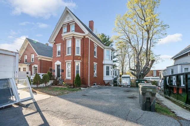 victorian house with a chimney, brick siding, and aphalt driveway