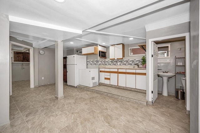 kitchen with a sink, freestanding refrigerator, backsplash, light countertops, and black microwave