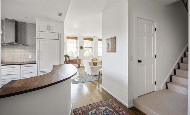 kitchen with backsplash, white cabinets, paneled fridge, and wall chimney range hood