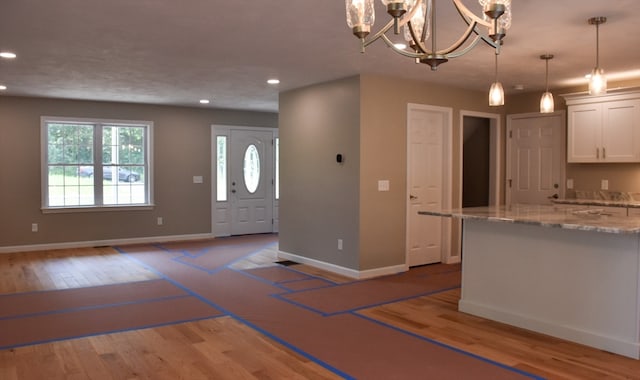 kitchen featuring white cabinetry, light hardwood / wood-style flooring, a chandelier, light stone counters, and decorative light fixtures