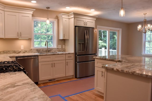 kitchen with appliances with stainless steel finishes, light stone counters, decorative light fixtures, white cabinetry, and a sink