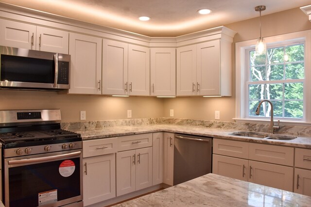 kitchen with white cabinetry, stainless steel appliances, light stone countertops, decorative light fixtures, and sink