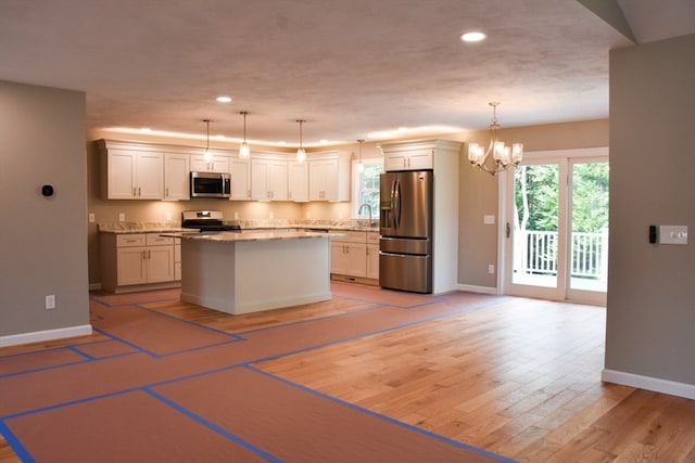 kitchen with a chandelier, white cabinets, light wood-type flooring, a center island, and appliances with stainless steel finishes