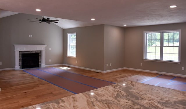 unfurnished living room featuring ceiling fan, light hardwood / wood-style floors, a tiled fireplace, and plenty of natural light