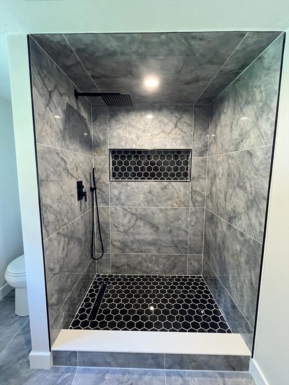 bathroom featuring toilet, baseboards, and tiled shower