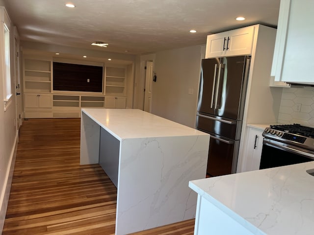 kitchen featuring white cabinets, light stone countertops, stainless steel appliances, wood-type flooring, and tasteful backsplash