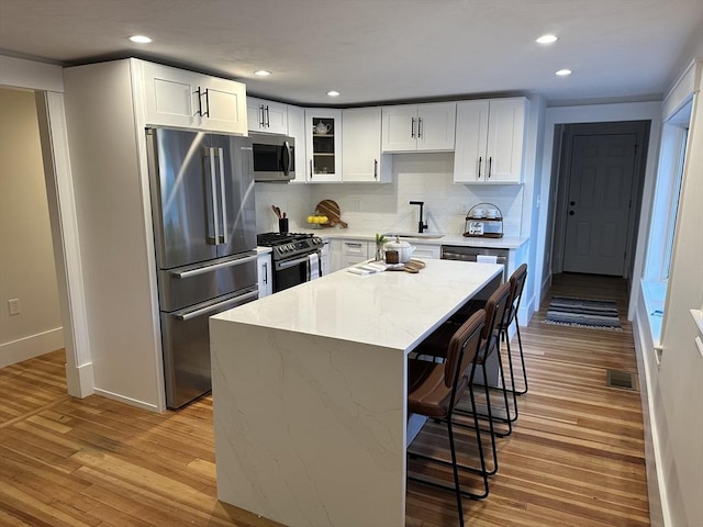 kitchen with visible vents, a kitchen island, glass insert cabinets, stainless steel appliances, and white cabinetry