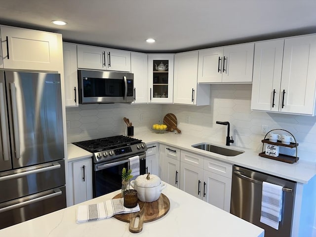 kitchen featuring backsplash, appliances with stainless steel finishes, glass insert cabinets, white cabinets, and a sink