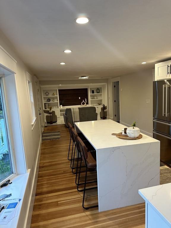 kitchen featuring white cabinets, open floor plan, wood finished floors, a center island, and high end fridge