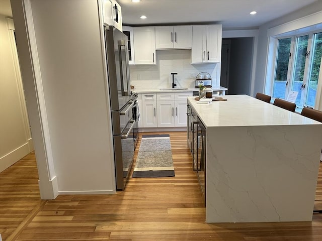 kitchen featuring light wood-style flooring, high end refrigerator, a sink, white cabinetry, and a center island