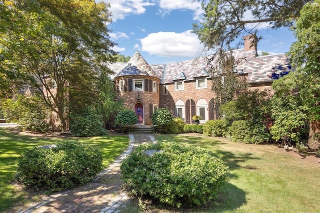 tudor house featuring a front lawn, a chimney, a high end roof, and brick siding