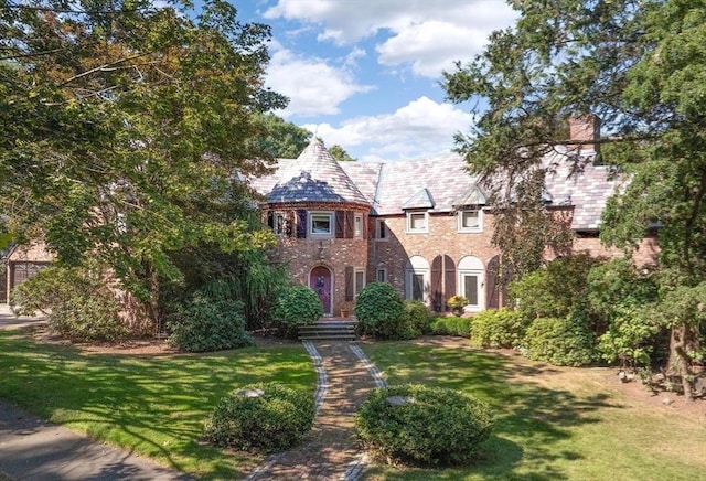 tudor house featuring brick siding, a chimney, a front yard, and a high end roof