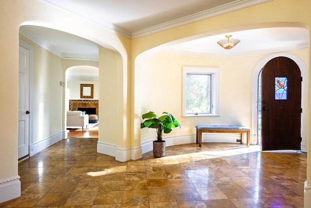 entrance foyer featuring arched walkways, ornamental molding, a fireplace, and baseboards