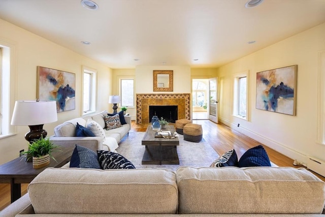 living room with baseboards, recessed lighting, a tiled fireplace, and light wood-style floors