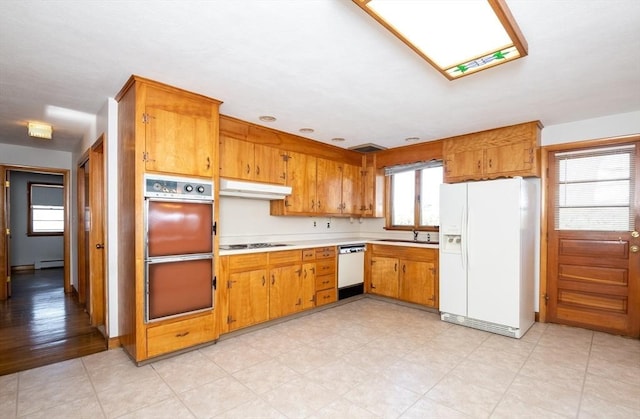 kitchen featuring under cabinet range hood, white appliances, a sink, light countertops, and brown cabinetry