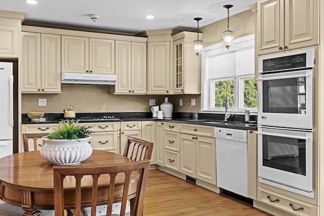61 Colonial Dr, Arlington, MA 02474 - kitchen with white appliances, cream cabinets, under cabinet range hood, dark countertops, and hanging light fixtures