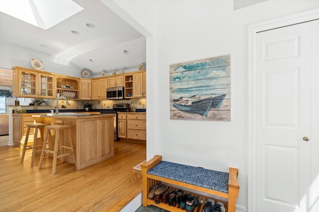 kitchen with a breakfast bar area, open shelves, glass insert cabinets, stainless steel appliances, and light wood-style flooring