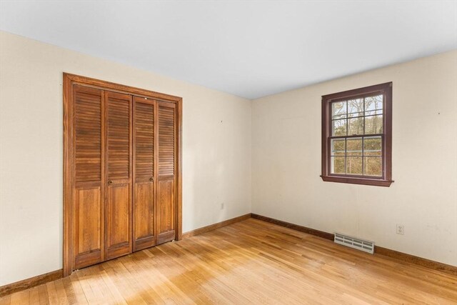 unfurnished bedroom with light wood-style flooring, a closet, visible vents, and baseboards