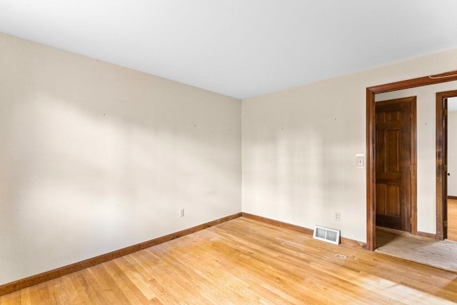 spare room featuring wood finished floors, visible vents, and baseboards