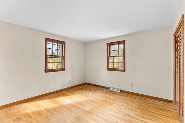 unfurnished room featuring a wealth of natural light, visible vents, light wood-style flooring, and baseboards