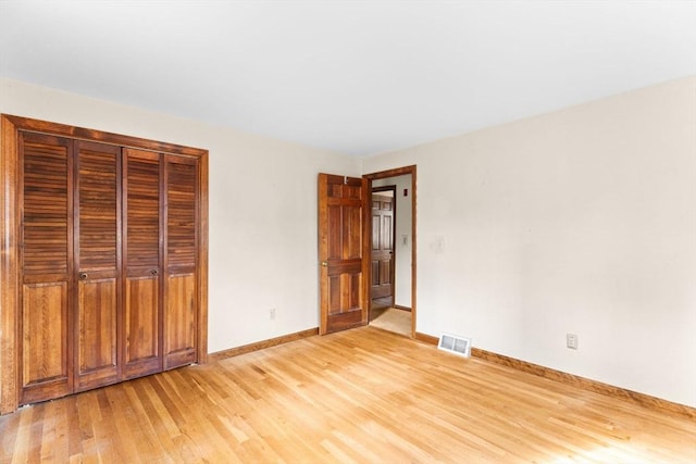 unfurnished bedroom with a closet, light wood-type flooring, visible vents, and baseboards