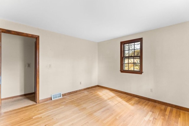 spare room featuring light wood-type flooring, visible vents, and baseboards