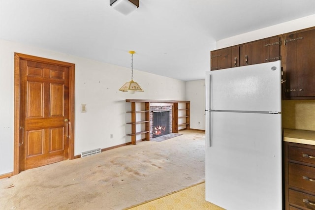 kitchen featuring visible vents, light countertops, a brick fireplace, freestanding refrigerator, and decorative light fixtures