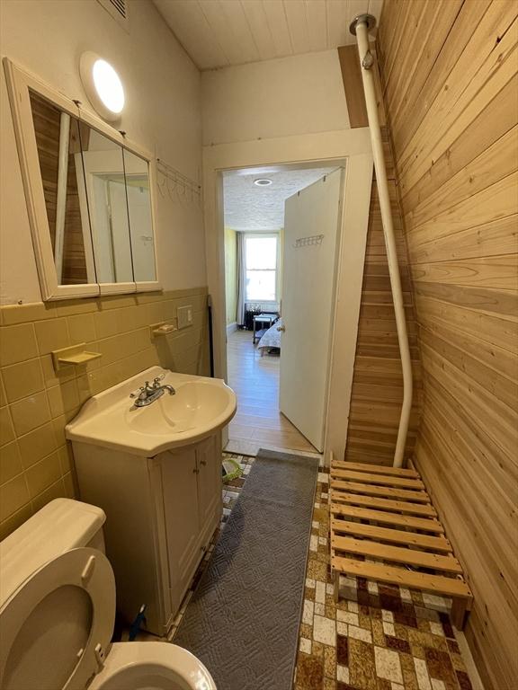 74 Newhall Unit 9, Lynn, MA 01902 - bathroom with wood walls, toilet, vanity, tile walls, and wainscoting