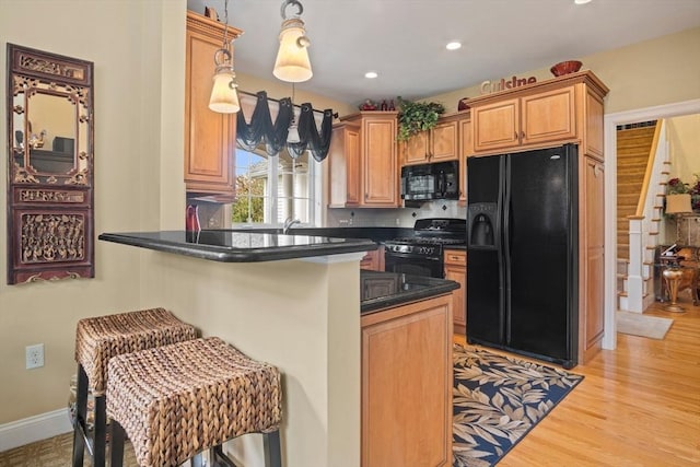 kitchen with hanging light fixtures, kitchen peninsula, a breakfast bar, and black appliances