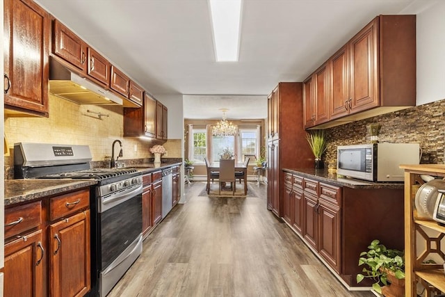 kitchen with under cabinet range hood, wood finished floors, a sink, a notable chandelier, and stainless steel appliances