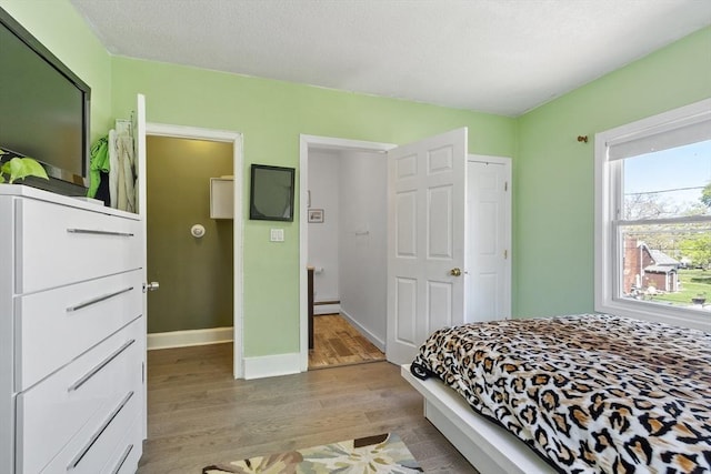bedroom with baseboards, a baseboard radiator, and light wood-style flooring