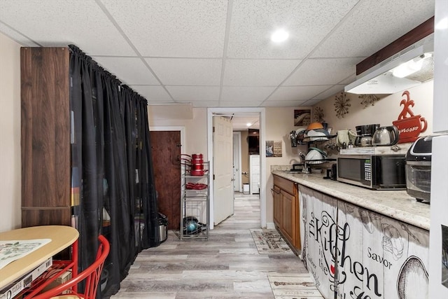 kitchen featuring light wood-style floors, light countertops, stainless steel microwave, and a drop ceiling