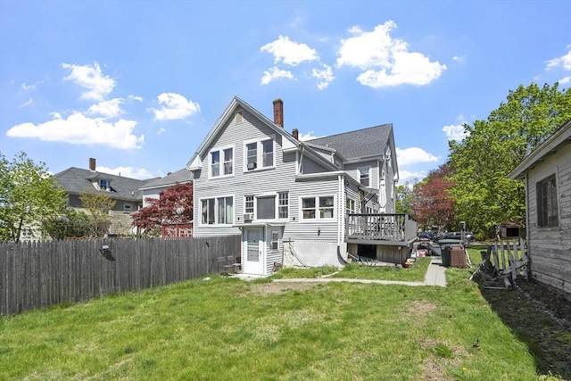 rear view of house featuring a lawn, fence, a chimney, and a wooden deck