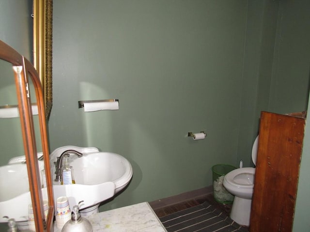 half bath featuring toilet, baseboards, and a sink