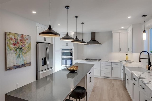 kitchen with stainless steel appliances, wall chimney range hood, white cabinets, and light hardwood / wood-style floors