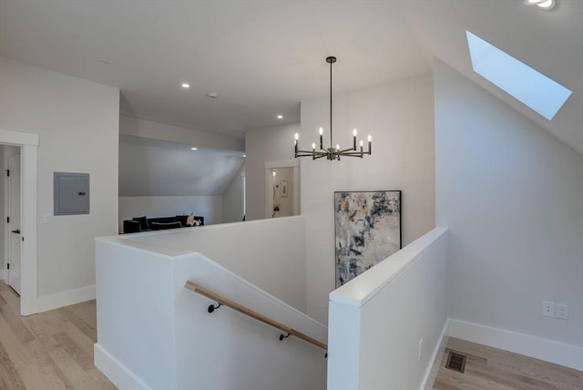 corridor with electric panel, an inviting chandelier, vaulted ceiling, and light hardwood / wood-style floors