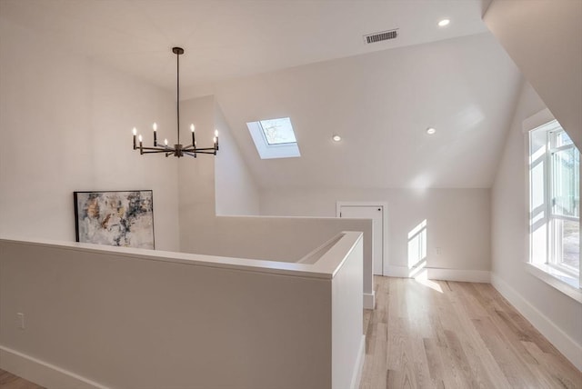 corridor with light hardwood / wood-style floors, vaulted ceiling with skylight, and a wealth of natural light