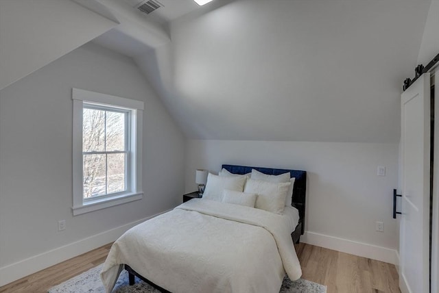 bedroom with vaulted ceiling, light hardwood / wood-style floors, and a barn door