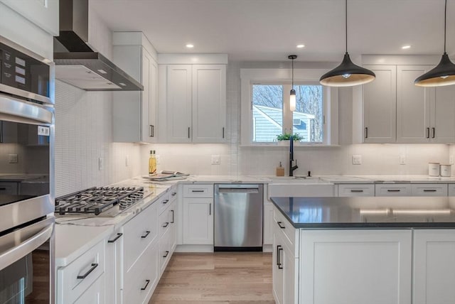 kitchen with white cabinets, wall chimney exhaust hood, light wood-type flooring, hanging light fixtures, and appliances with stainless steel finishes