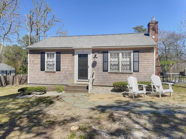 view of front of property featuring a patio, a shingled roof, a chimney, and fence